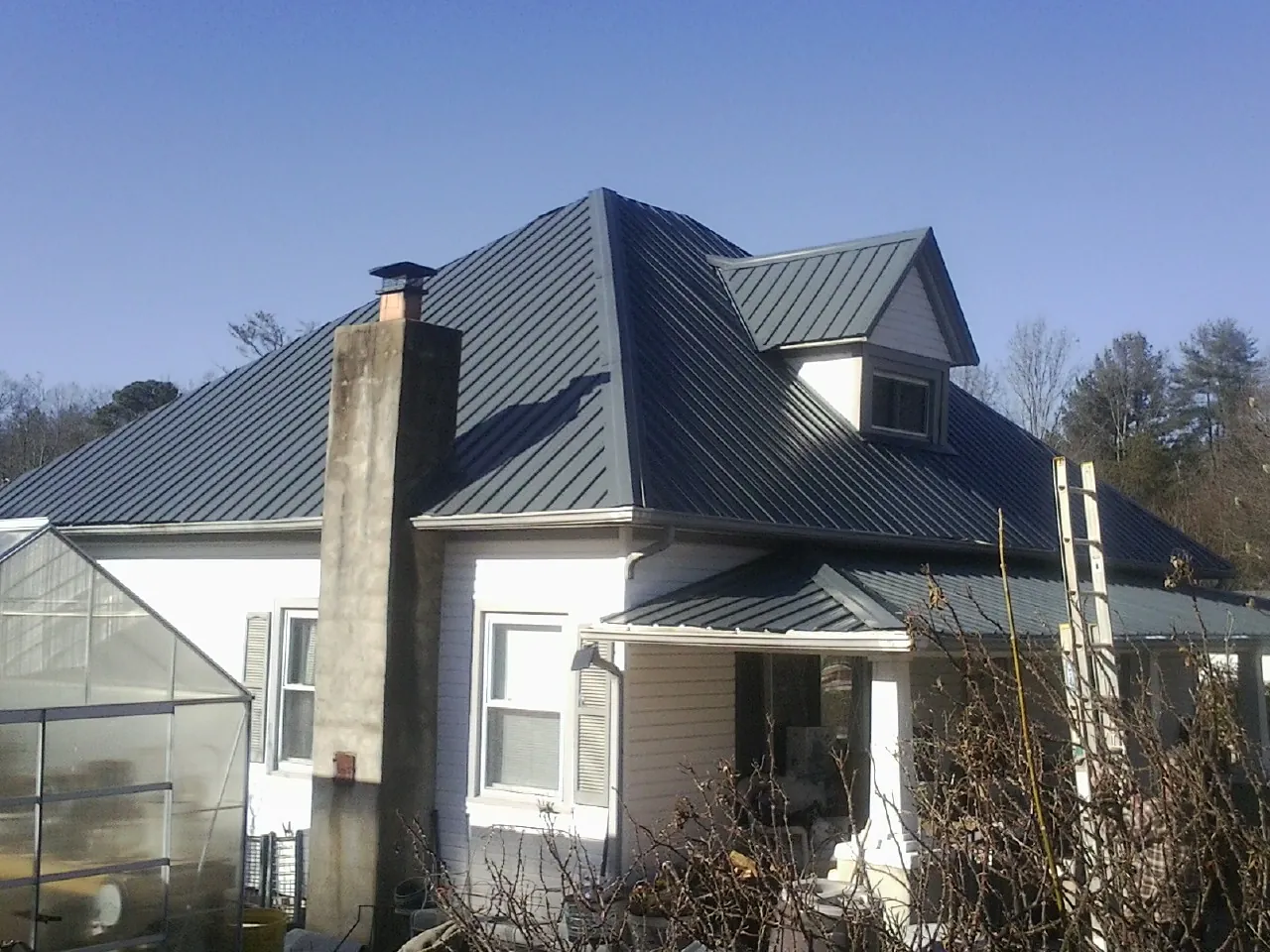 Dark blue standing seam metal roof on a white farmhouse with dormer — Slate & Tile Roof Repair by Roofing Brothers in Little Switzerland