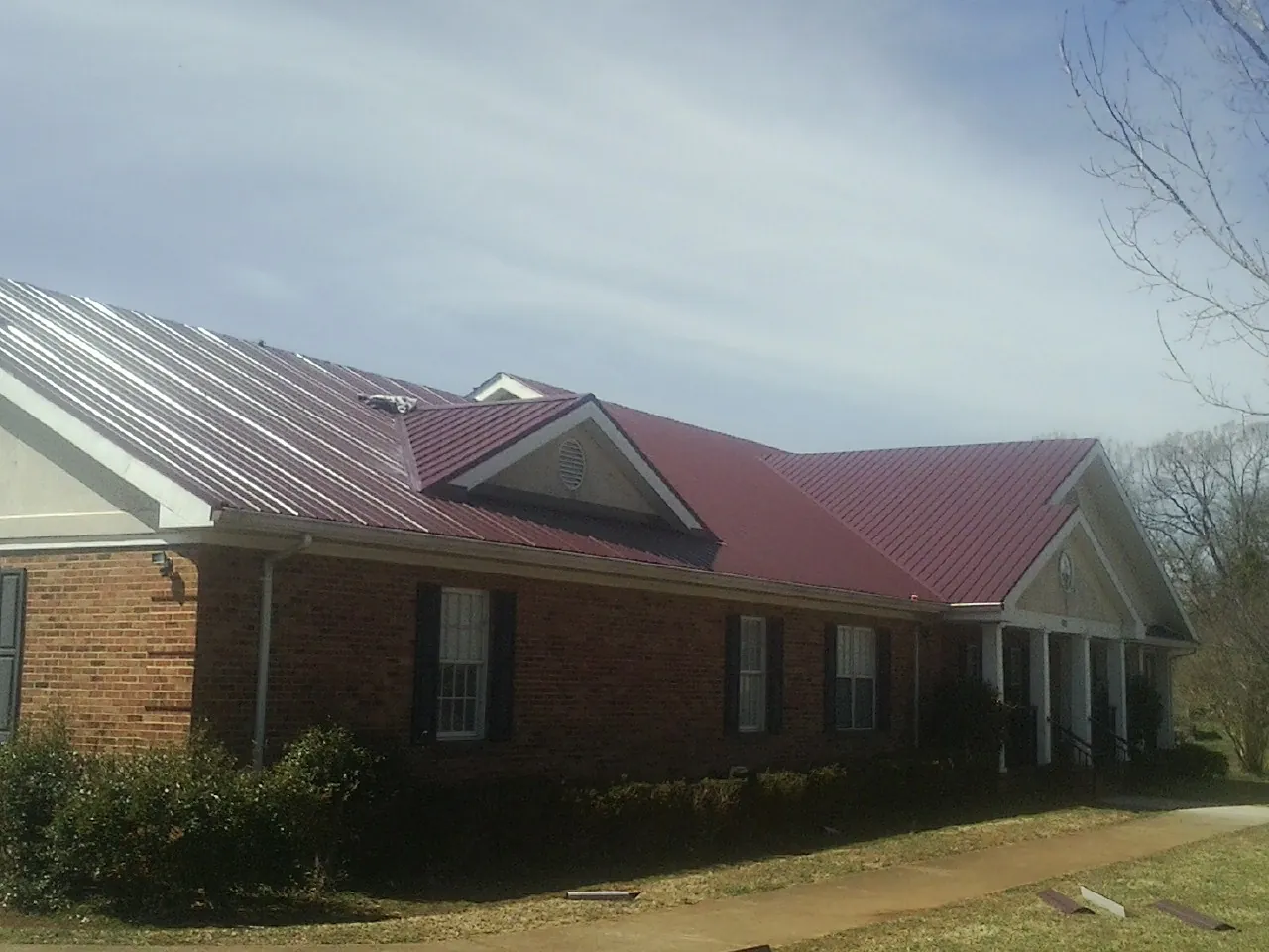 Red metal roof with gabled entries on a long brick building, from a Hail Damage Roof Repair job in Little Switzerland