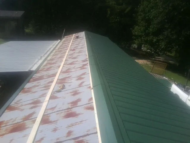 Old rusted panels beside newly installed green metal roofing — Wind Damage Roof Repair by Roofing Brothers in Little Switzerland