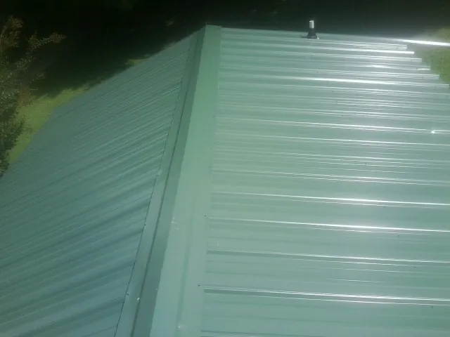 New green metal panels meeting at the ridge of a roof — Flat Roof Repair work by our crew in Little Switzerland