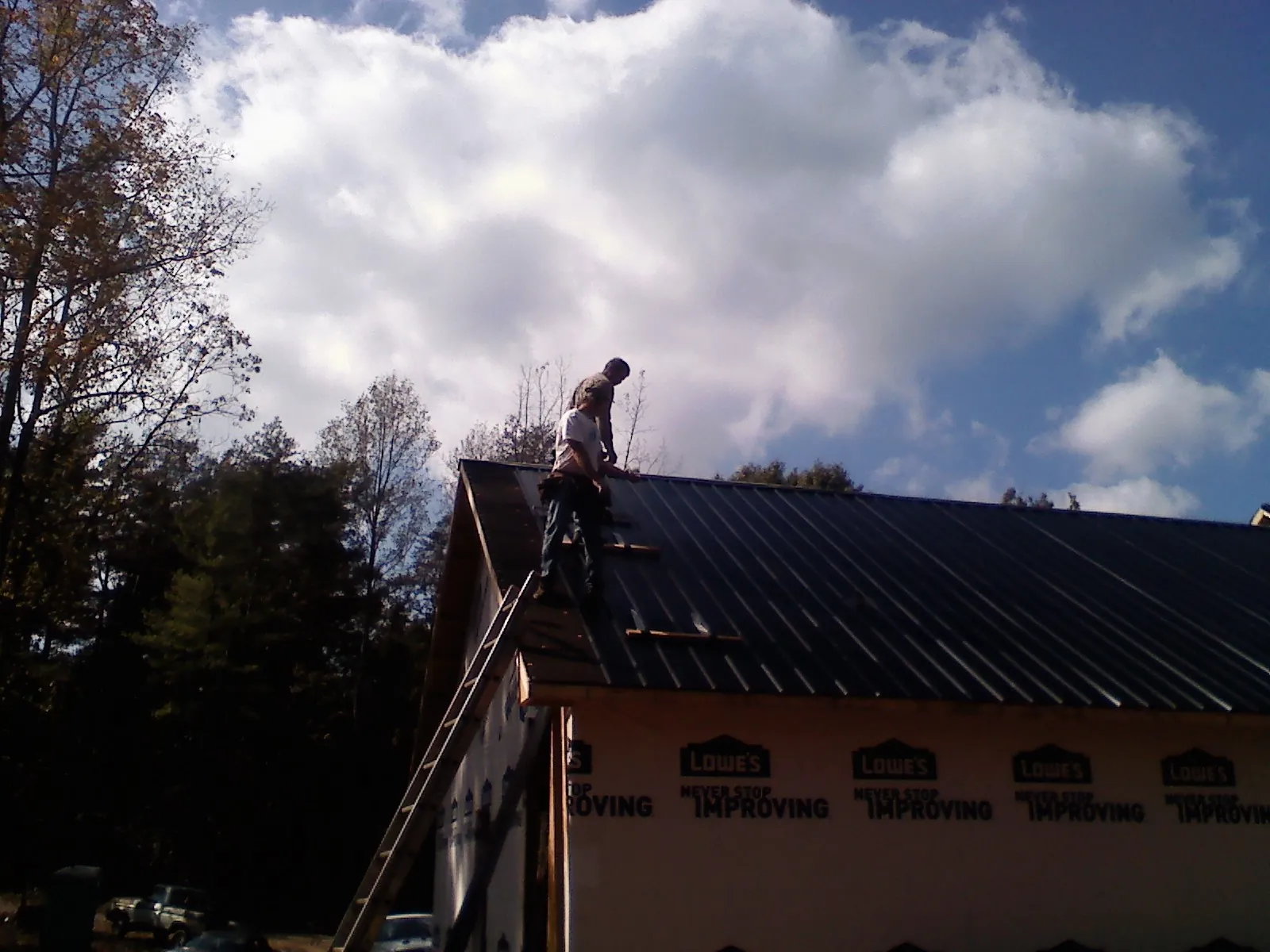 Roofer fastening dark metal panels high against a cloudy sky, from a Roof Inspection job in Little Switzerland