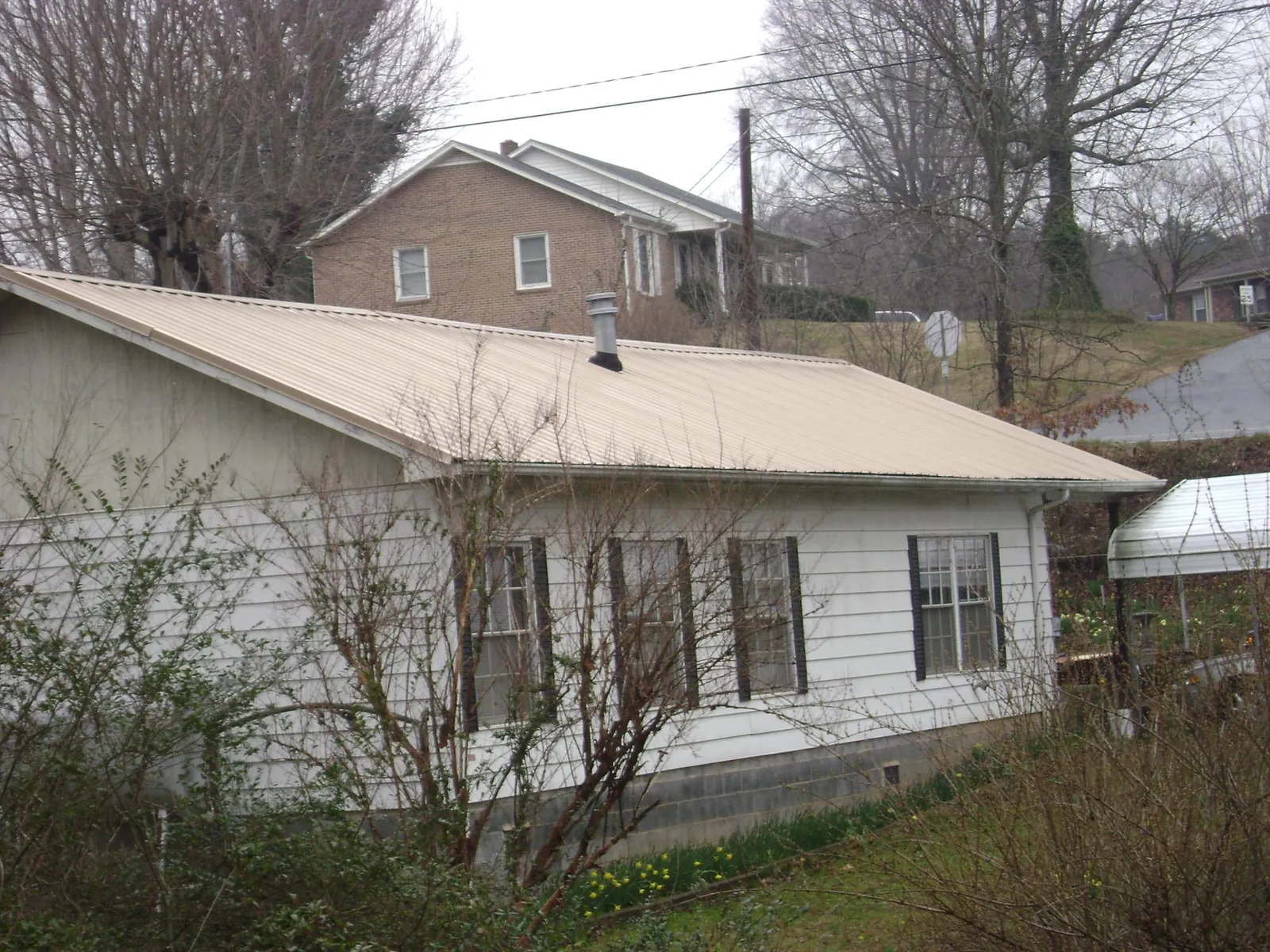 Tan metal roof on a white sided house set into a hillside — Commercial Roofing by Roofing Brothers in Little Switzerland