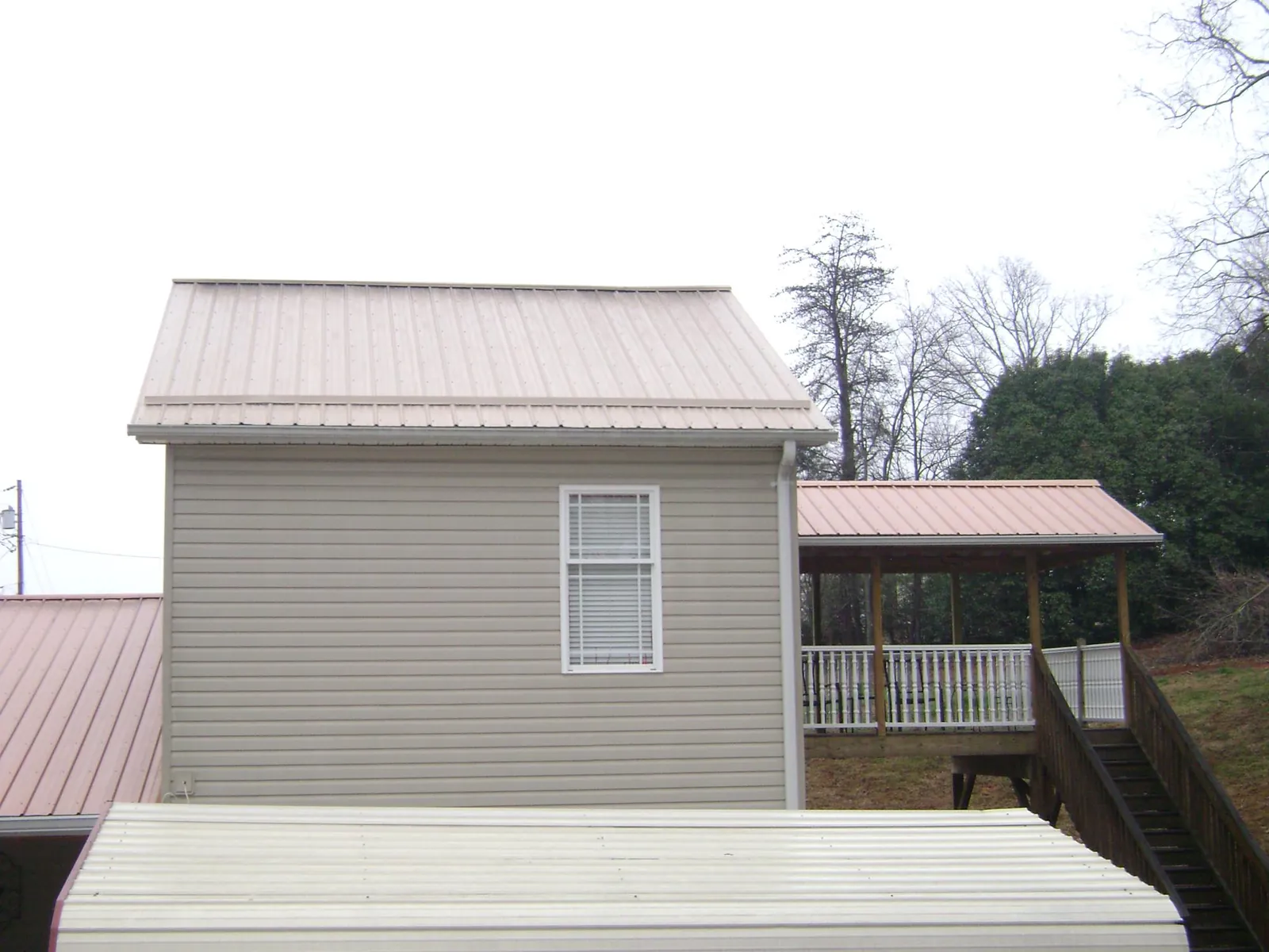 Tan metal roofs on a two story addition and attached porch, from a Roof Replacement job in Little Switzerland